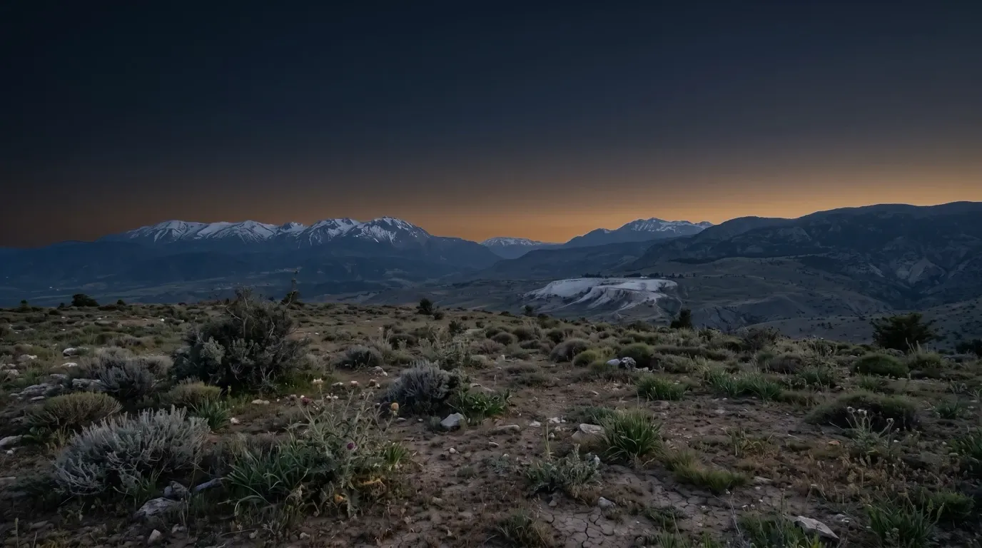 A long valley below snow-capped mountains, white travertine terraces far off on the slope.