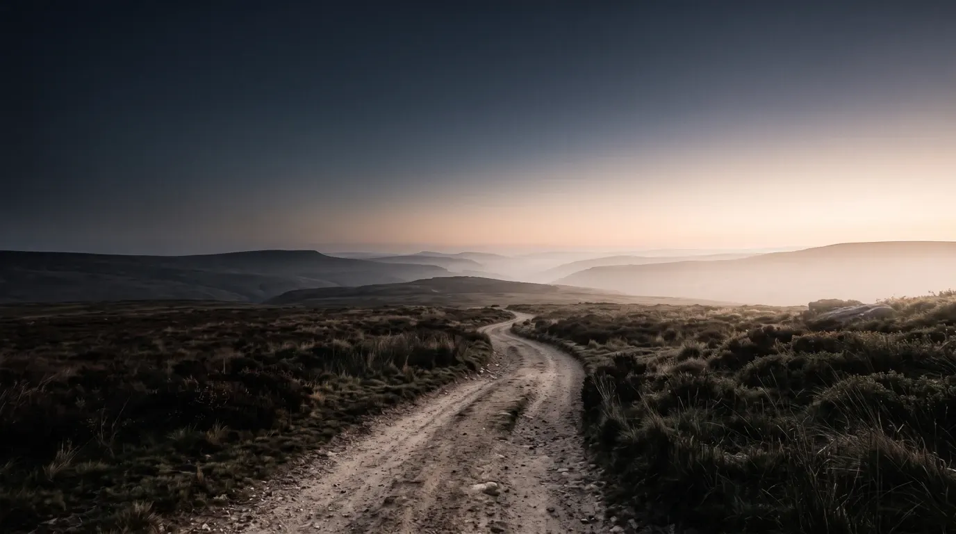 A dry road winding through empty hill country at first light, the way ahead dissolving into bright haze.