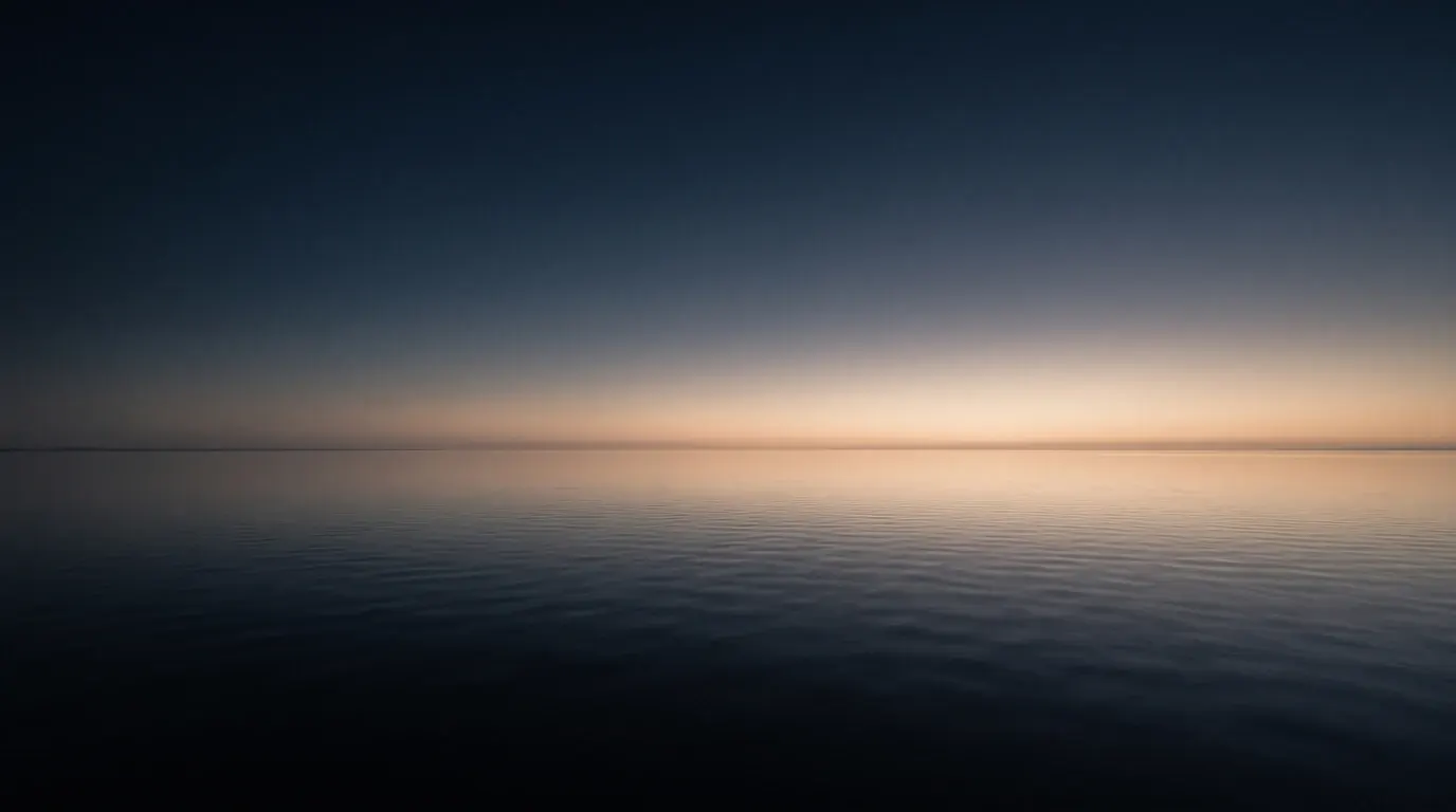 First light spreading across still water, the horizon barely separated from the sky.