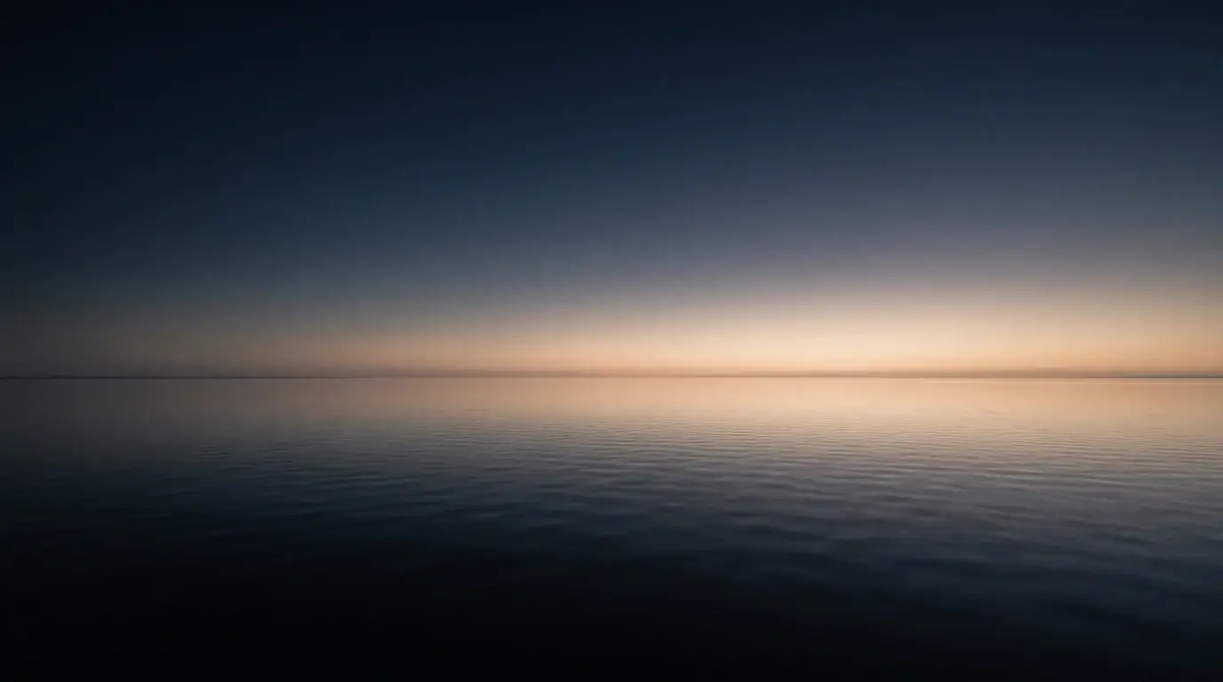 First light spreading across still water, the horizon barely separated from the sky.