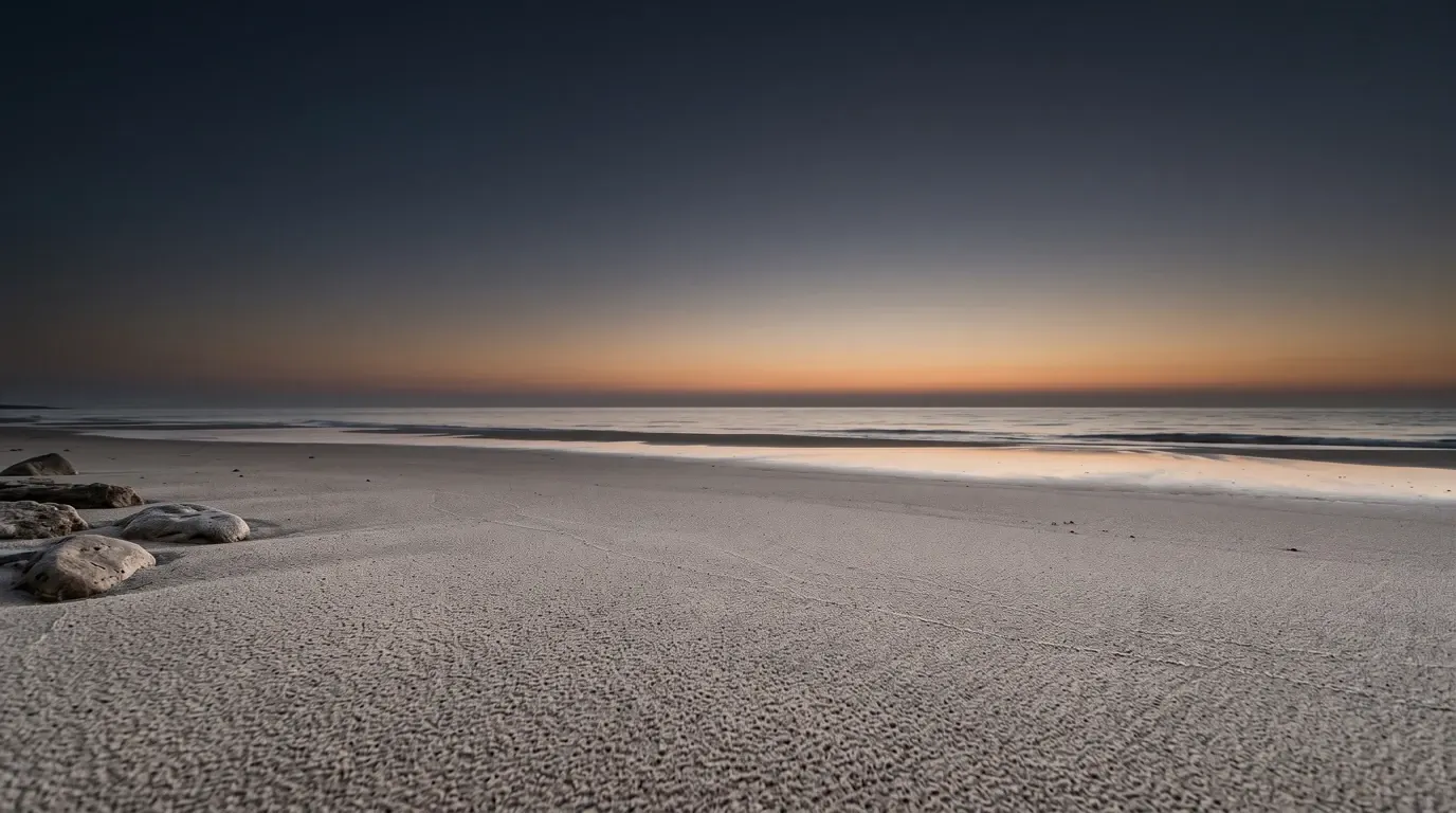 A wide shore of fine sand running to a flat sea, the grains beyond counting.