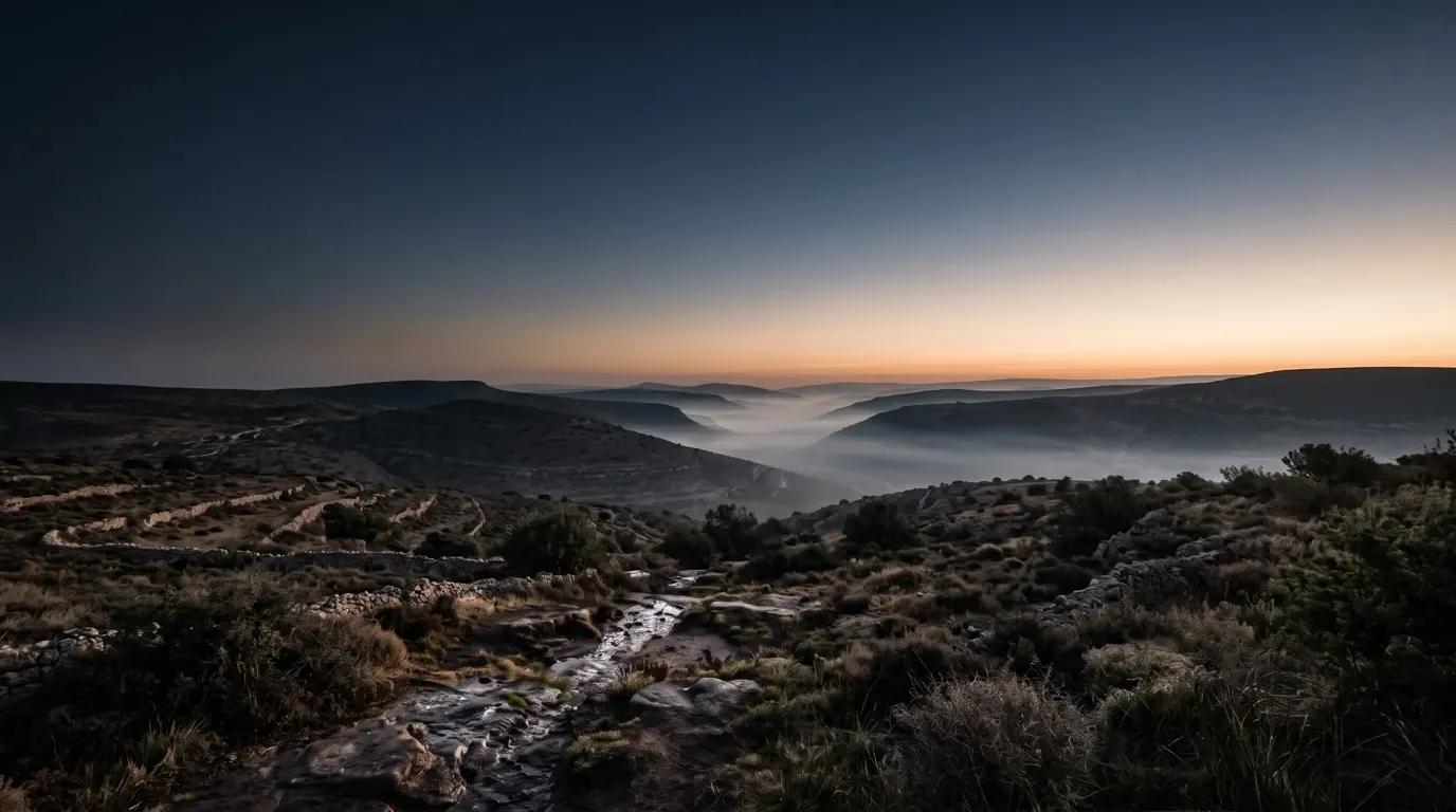 Mist lying in a valley before dawn, the hills around it still dark.