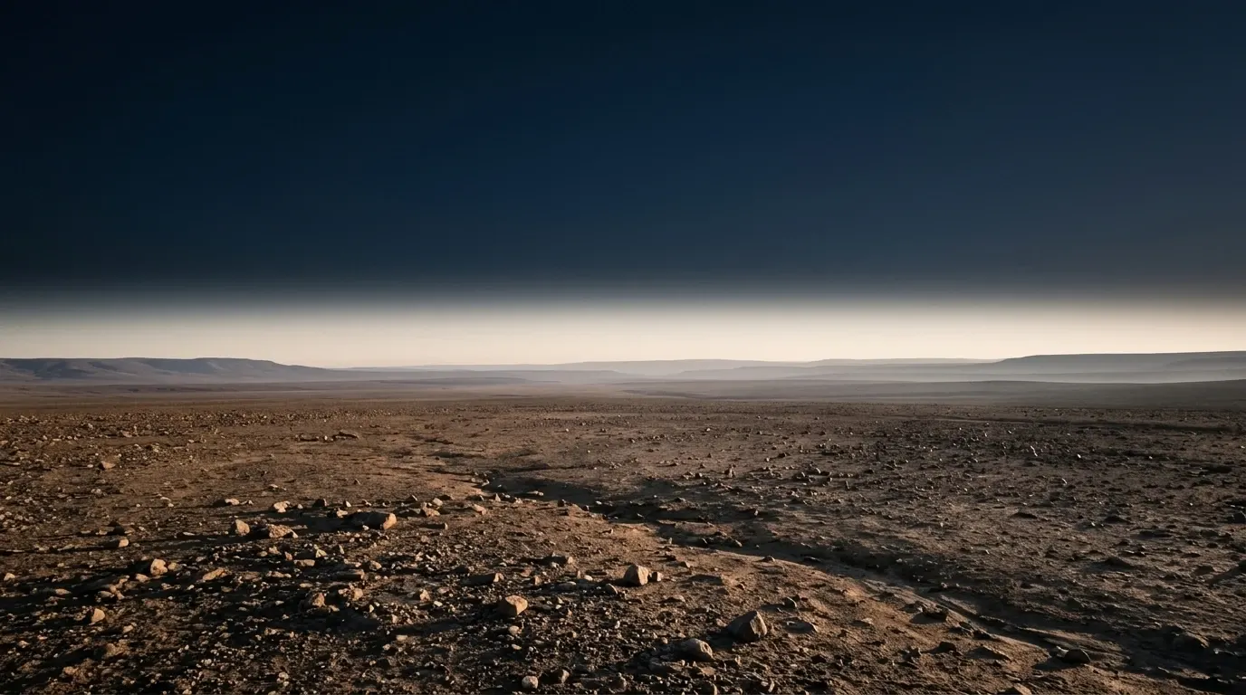 A wide floor of stony beaten earth scattered with loose stones, running flat to a far horizon.