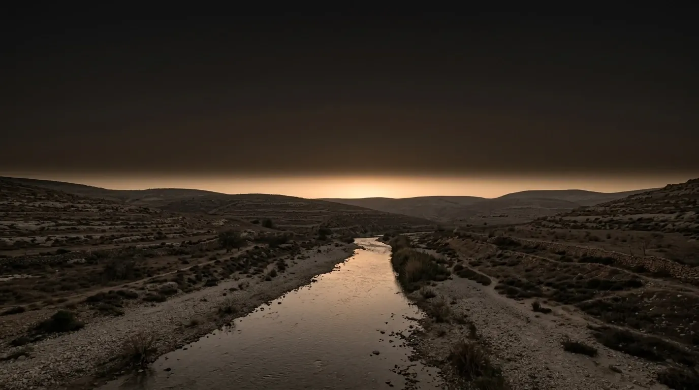 A broad shallow river running between low banks of pale gravel and thin dry scrub, the water still enough to hold the sky.
