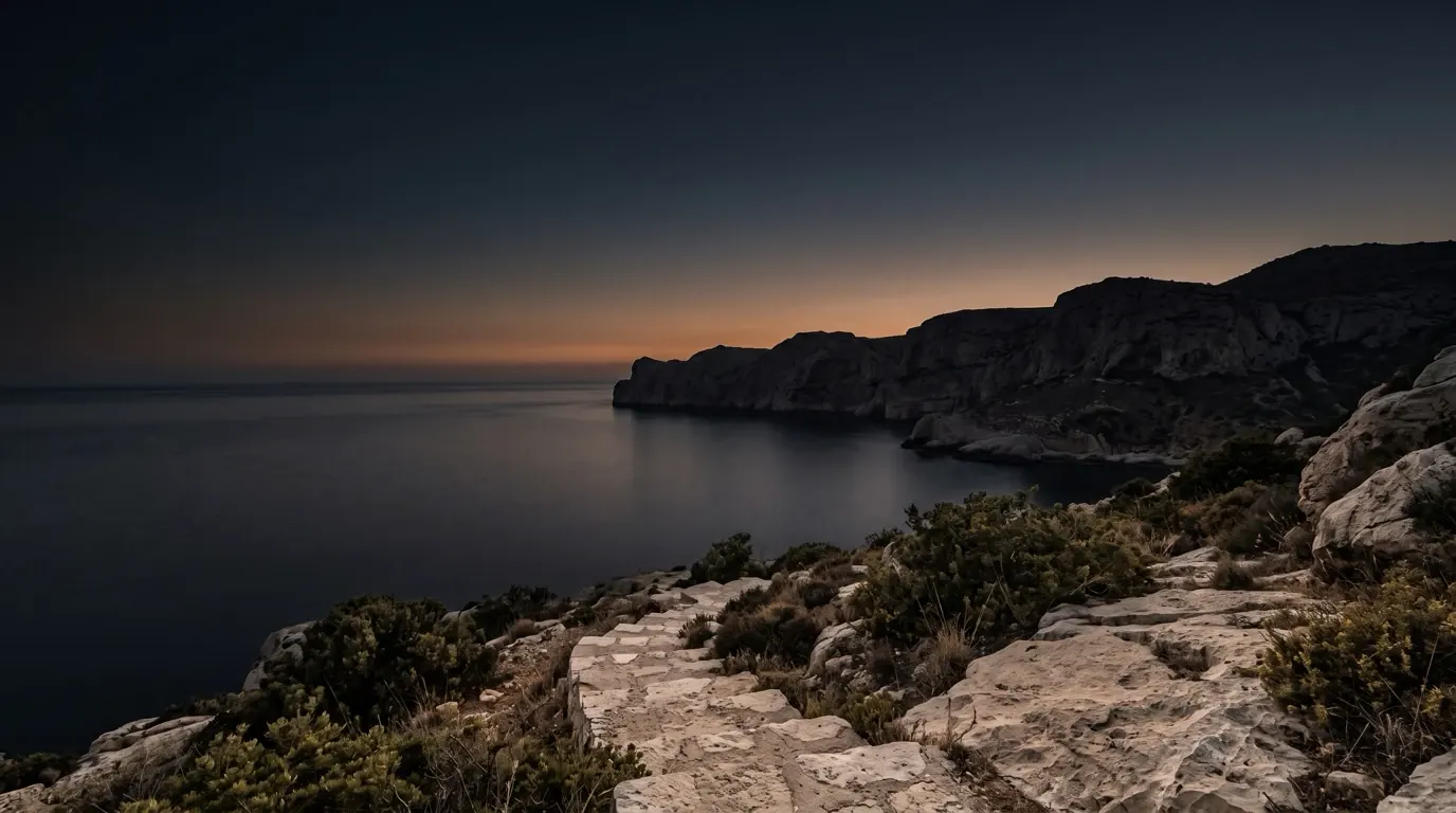 Une mer calme retenue au pied de falaises sombres, l’eau immobile tout le long du rivage.