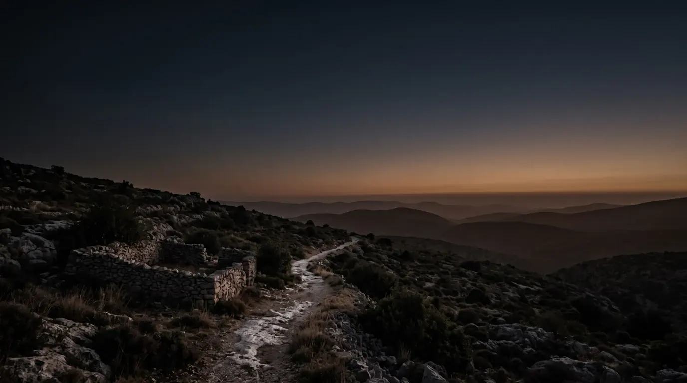 A lone path climbing into the mountains, a stone sheepfold left behind on the slope below.