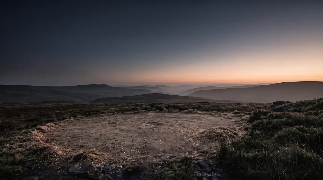 An open threshing floor of swept earth on a bare ridge, chaff drifted along its edge.