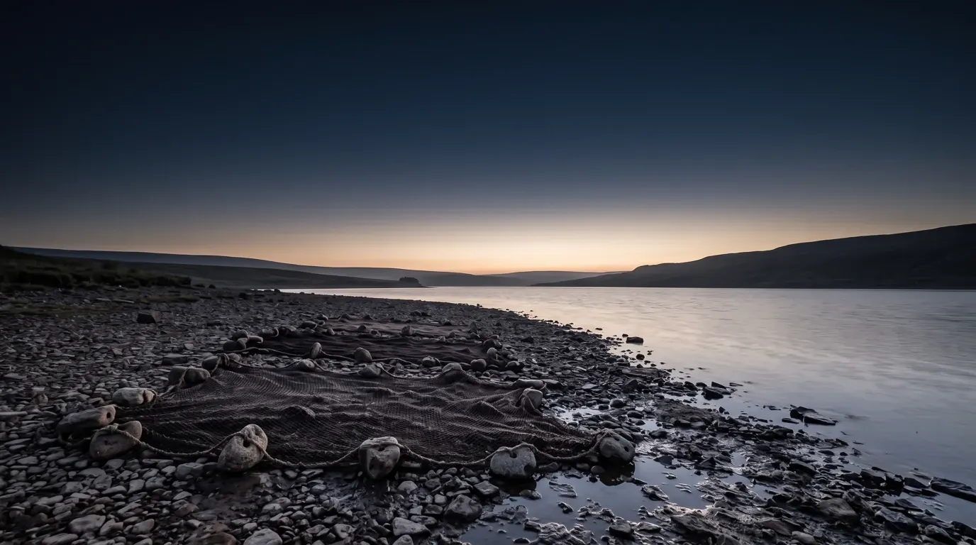 Knotted fishing nets spread to dry on a stony lake shore, weighted with pierced stones.