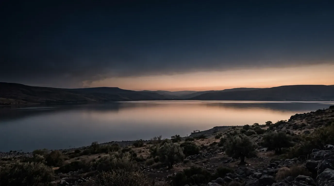 A wide lake gone flat and calm under breaking storm clouds.