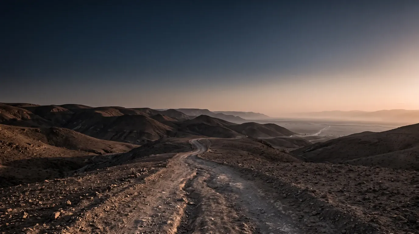 A dry stony road winding down through bare desert hills toward a wide plain.
