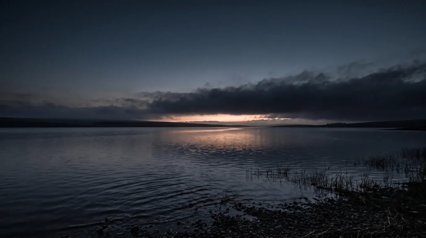 A wide inland lake seen from a stony shore, the far hills low on the horizon.