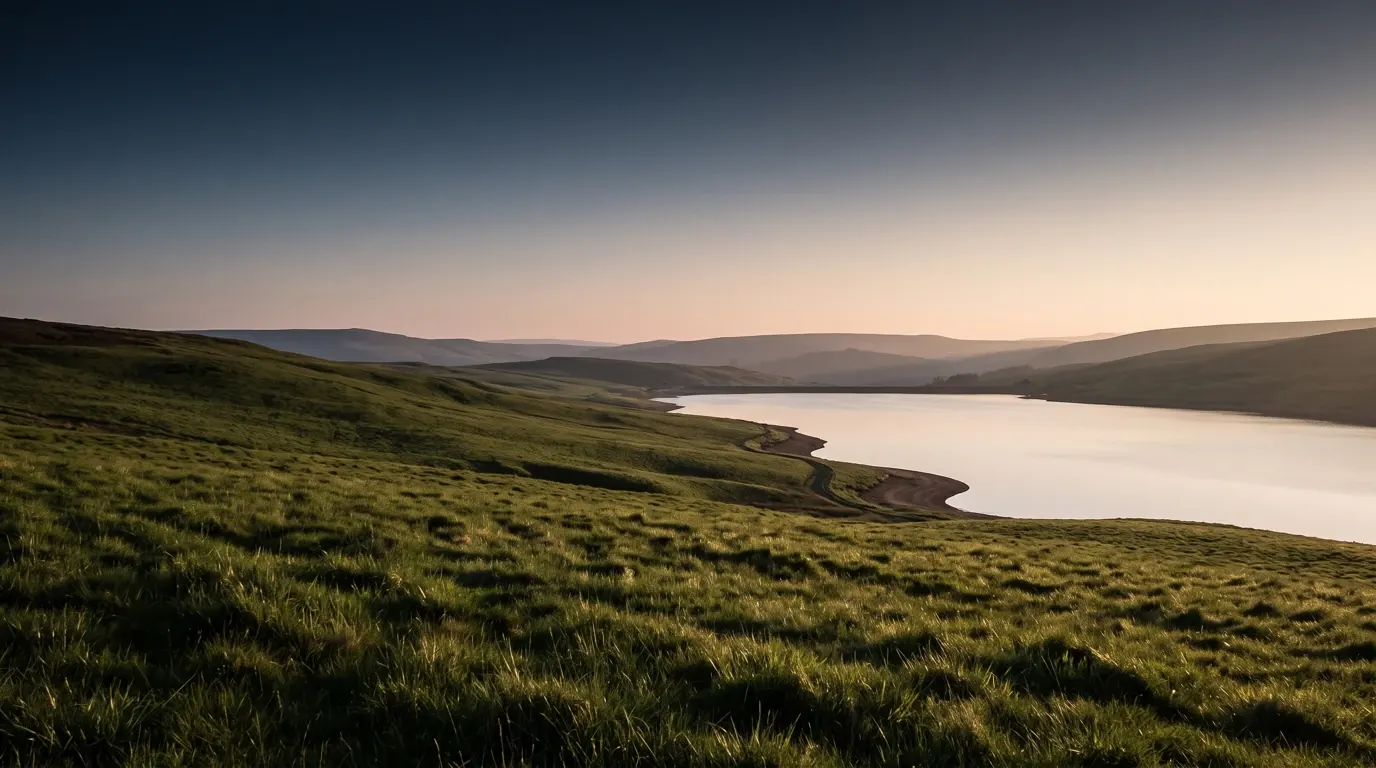 An open hillside of deep green grass sloping down to still water.