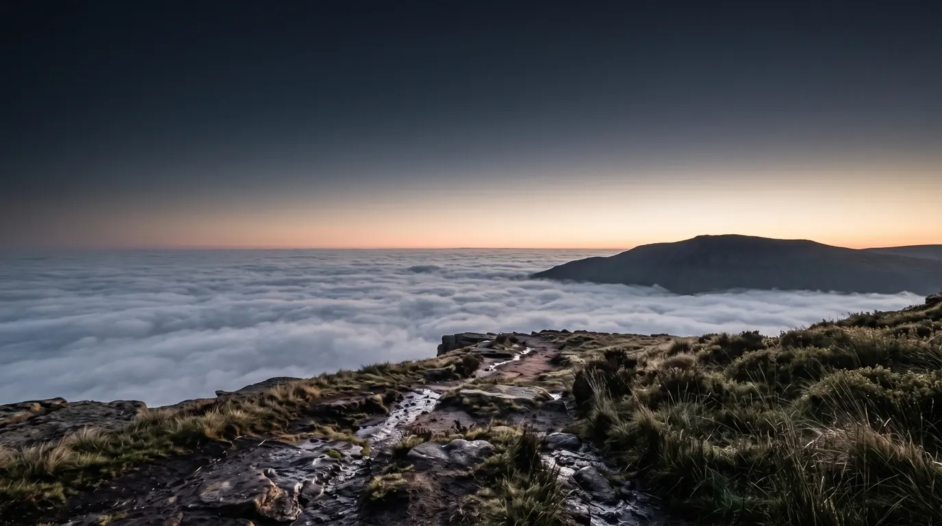 A bare mountain shoulder standing above a level sea of cloud.
