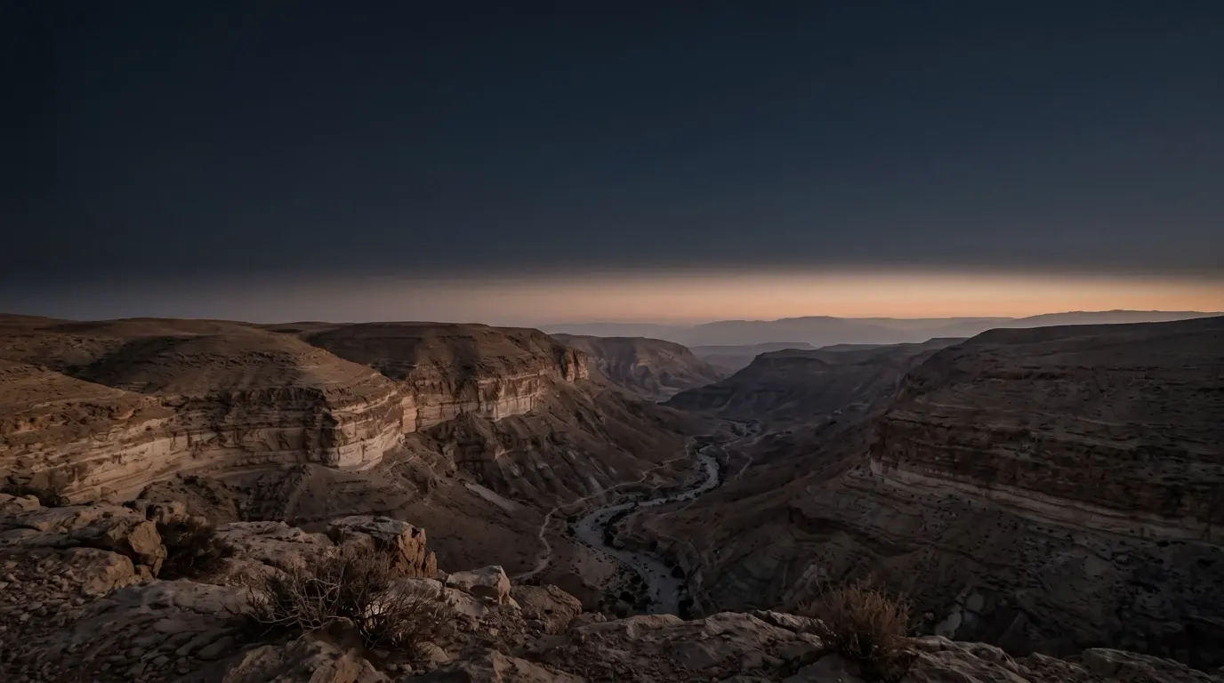 Layer upon layer of sedimentary rock exposed in the walls of a deep desert canyon, a thin stream far below.
