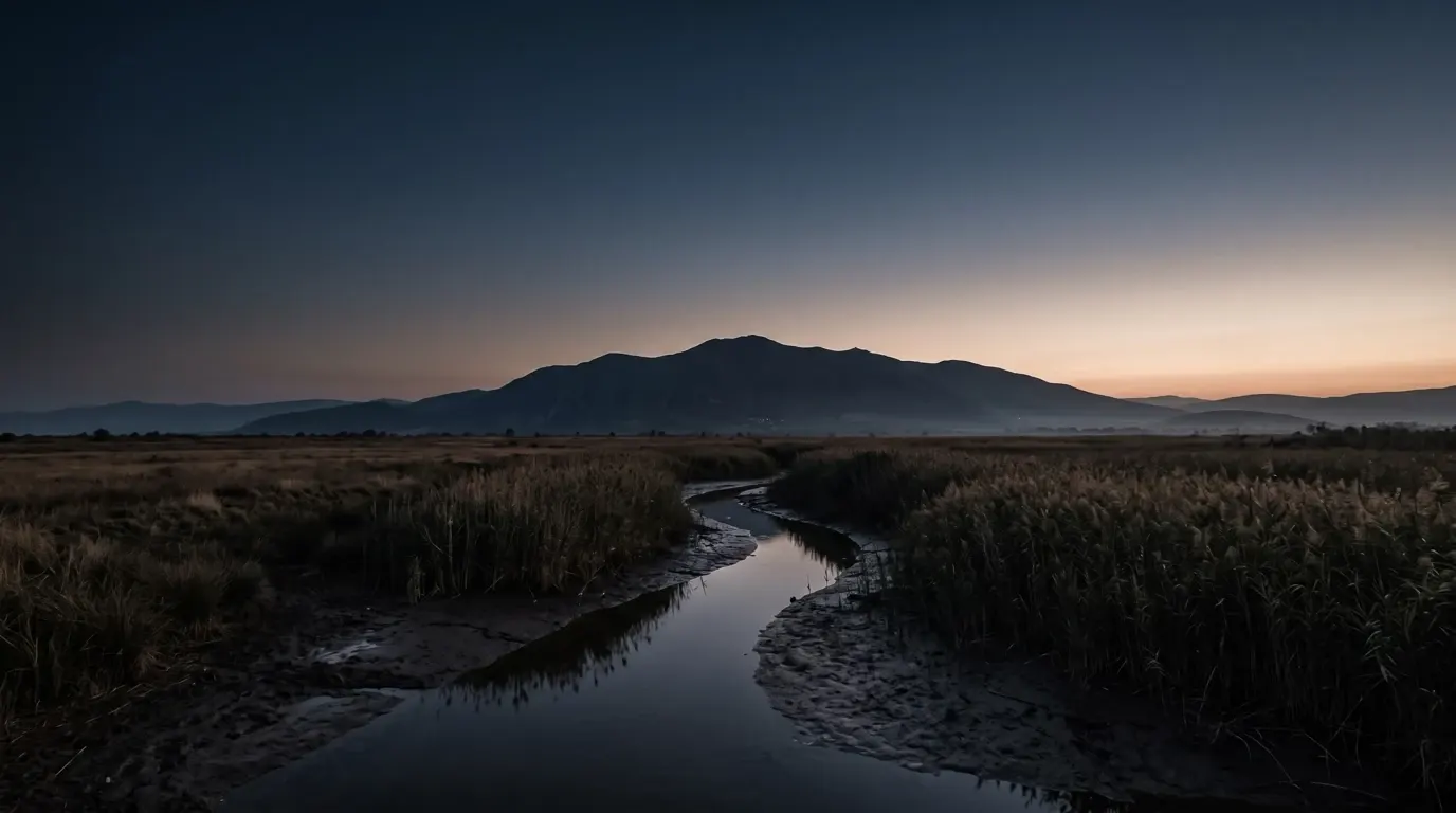 A small river among reeds on a wide plain below a great mountain.