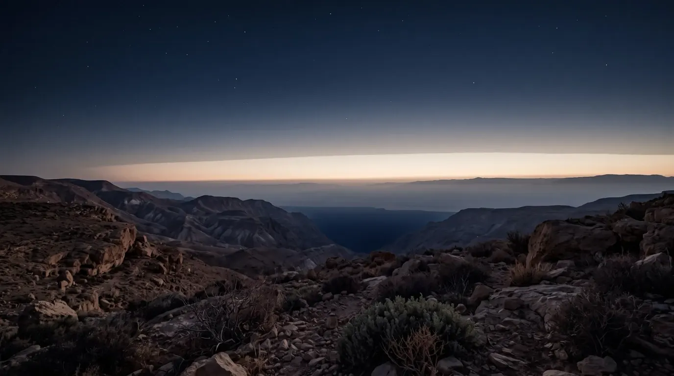 A long band of first light along the horizon above desert ridges.