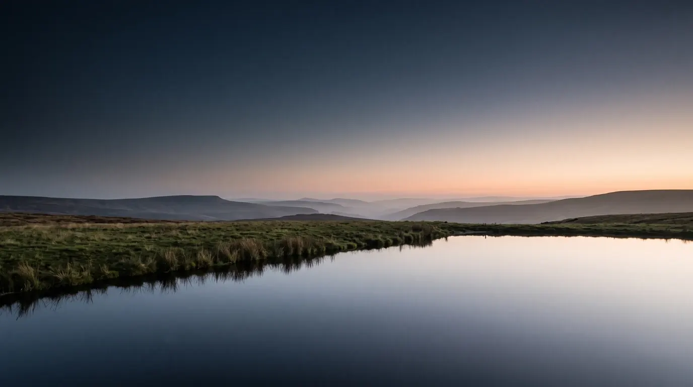 Still water lying unbroken at the low edge of a green pasture, the light level and late.
