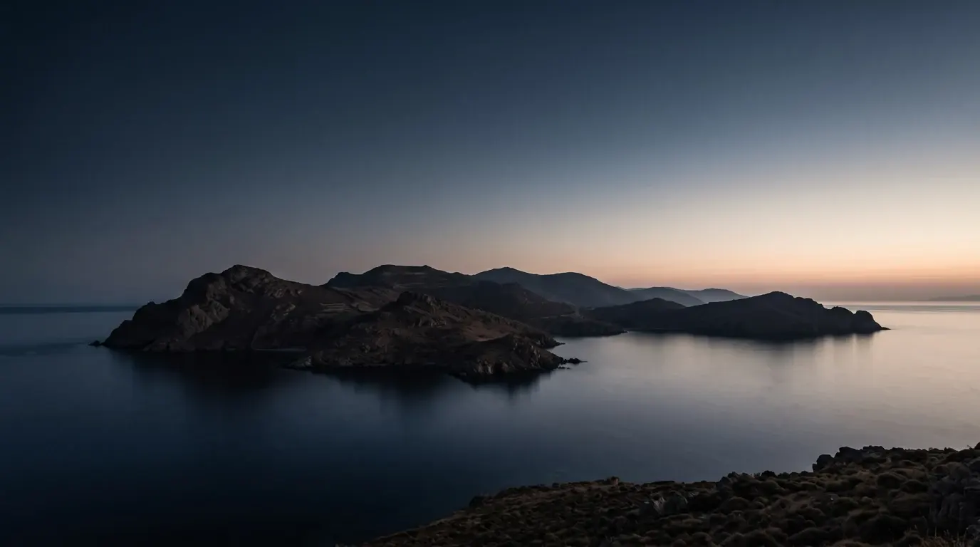 A rocky island with dark bare hills rising from a calm sea.