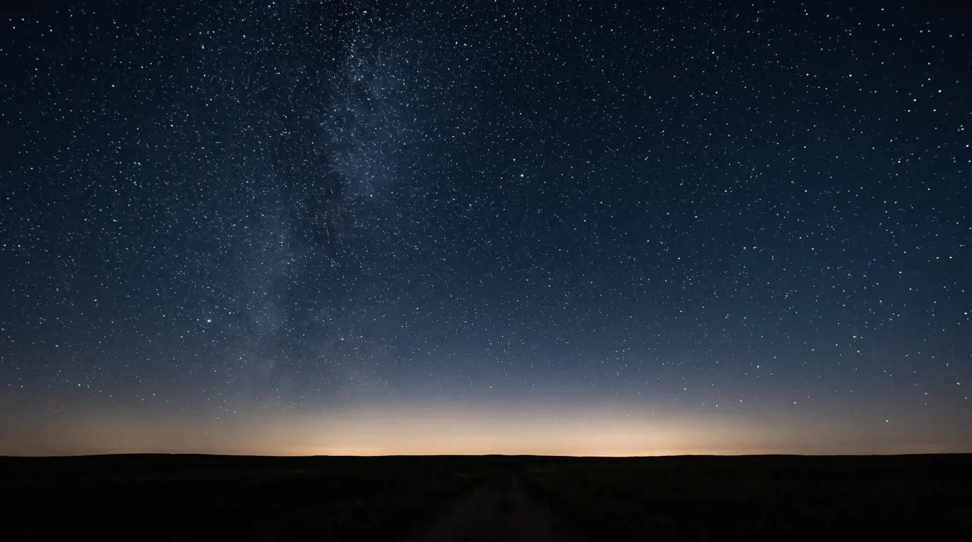 A night sky over flat empty country, more stars above the horizon than the eye can separate.