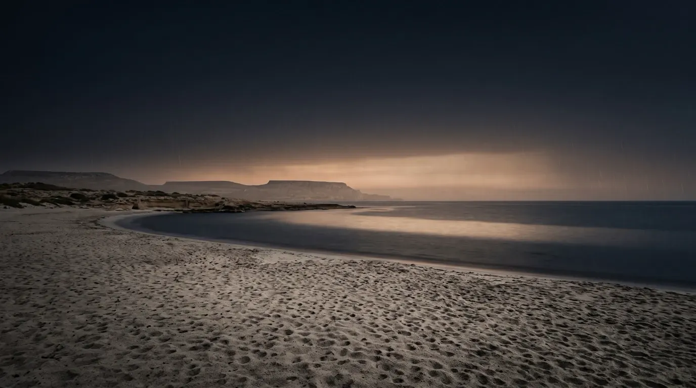 Fine rain falling on a wide sandy shore, each drop marking the sand.