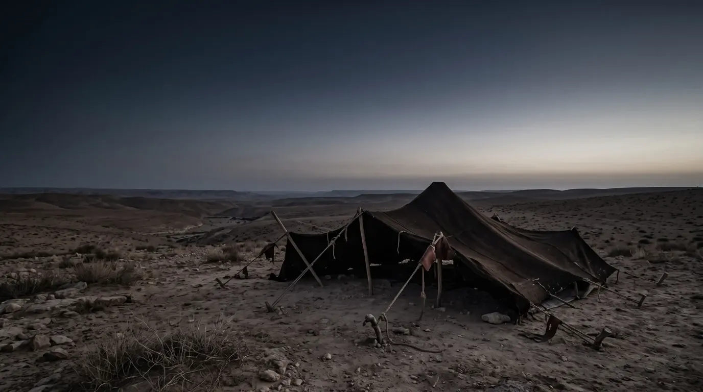 A dark goat-hair tent being struck on open desert ground, its poles leaning.